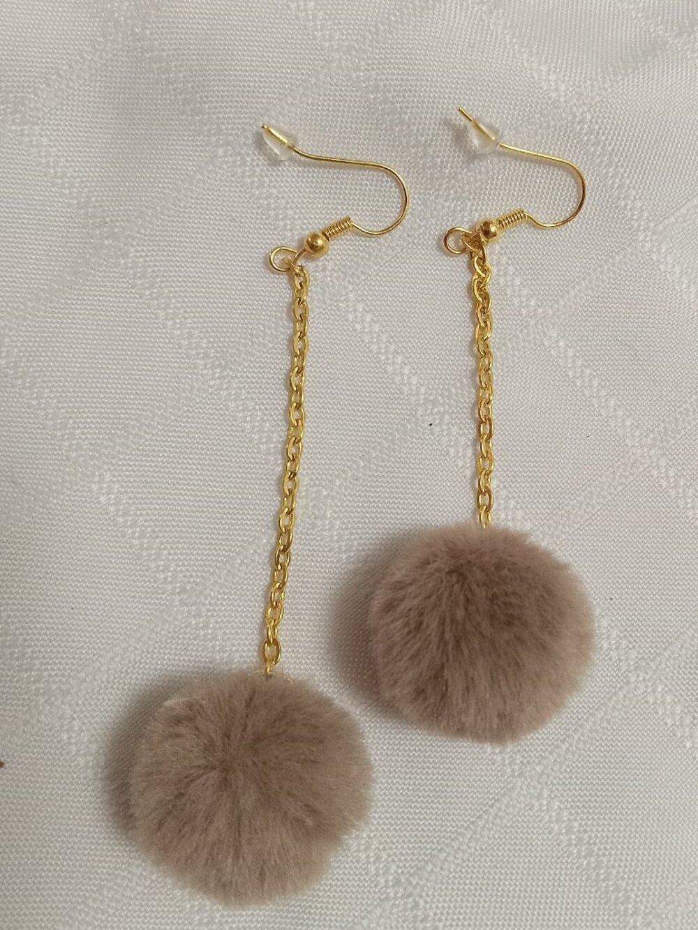 Handmade earrings with small pom-poms and gold-colored accent hooks and chains